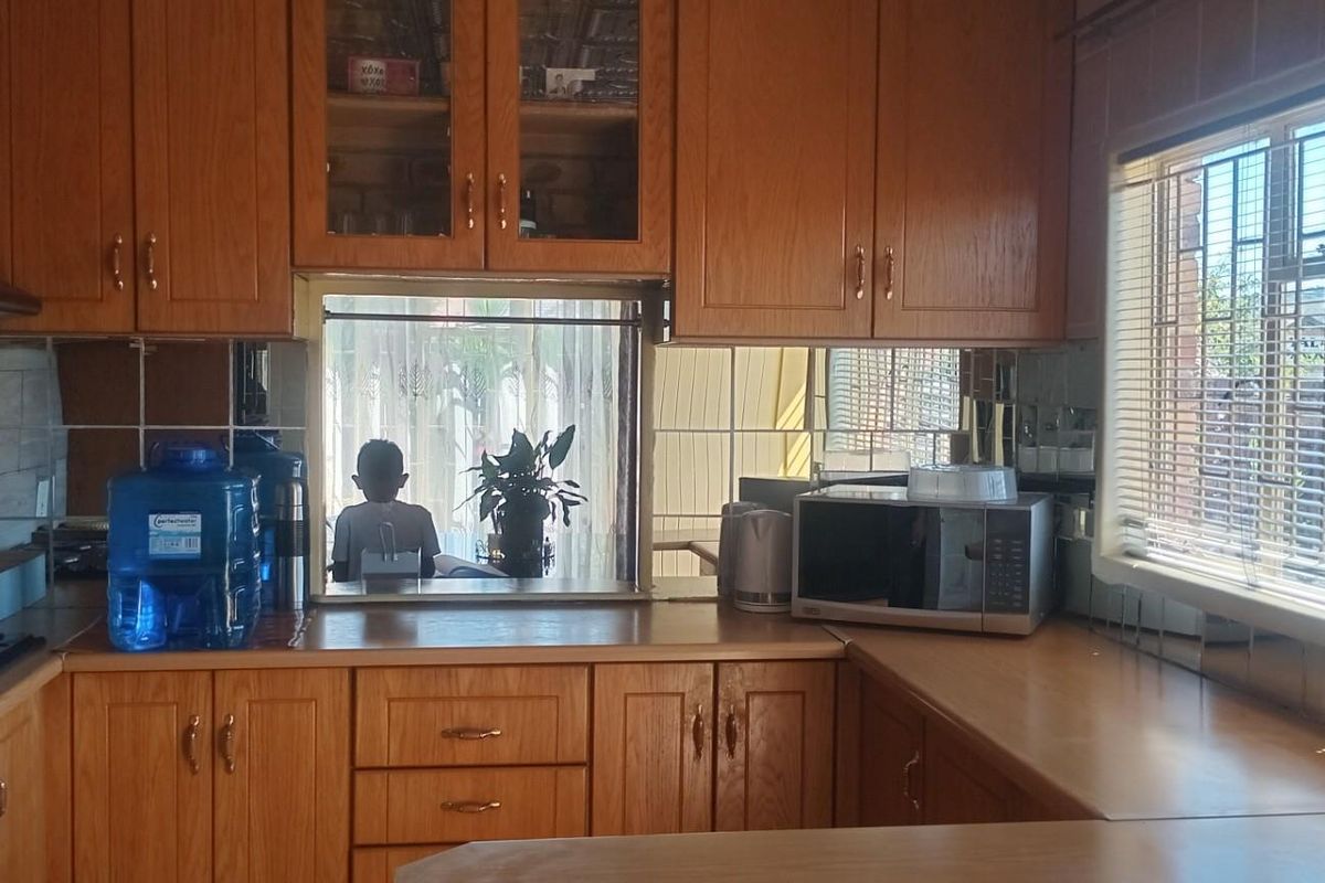 A traditional kitchen featuring wood-finish cabinetry, built-in oven, and a window with security bars, offering a functional layout with ample storage space.