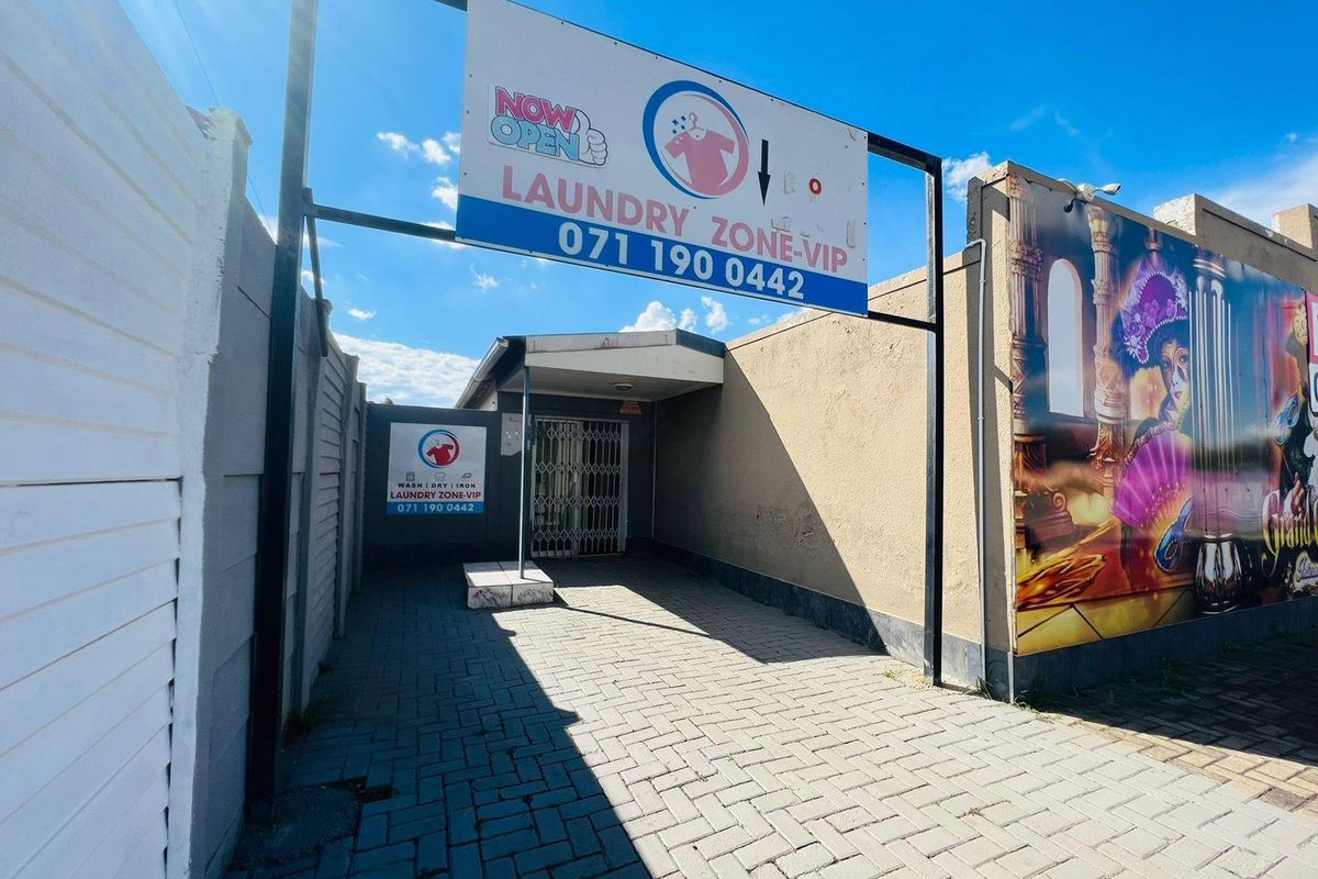 Exterior view of a commercial laundry facility entrance featuring paved access, security gate, and prominent business signage.