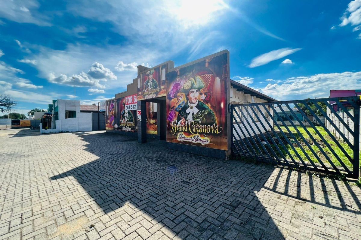 Front exterior view of a commercial property featuring paved driveway access, security gate, and prominent signage for an internet lounge.