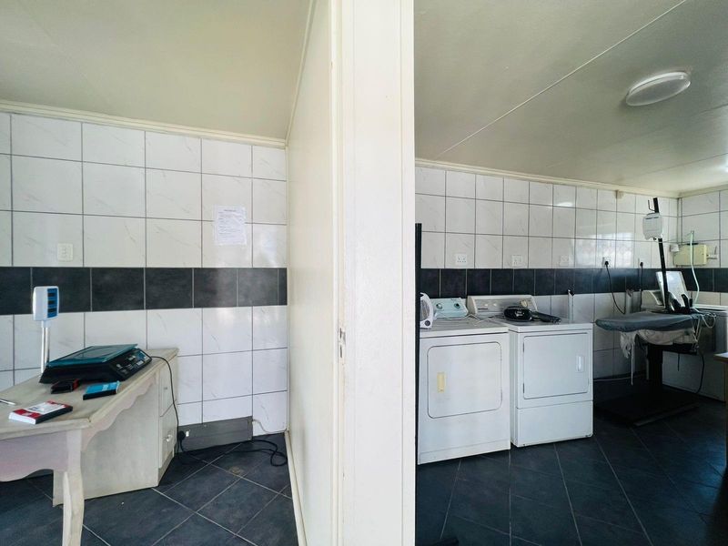 A functional laundry and utility area featuring tiled walls, dark floor tiles, and dedicated space for washing and drying appliances.
