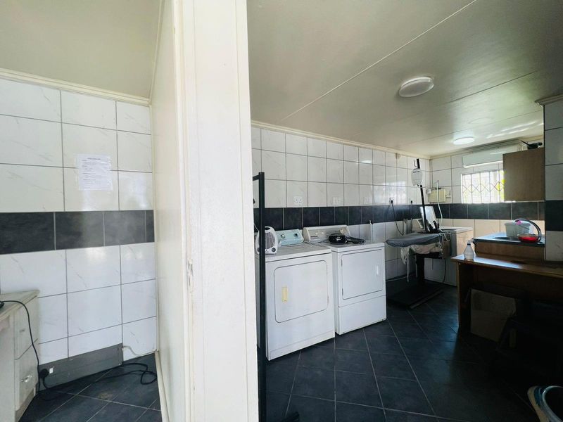 A functional laundry area featuring tiled walls, dark floor tiles, and dedicated space for washing and drying appliances.