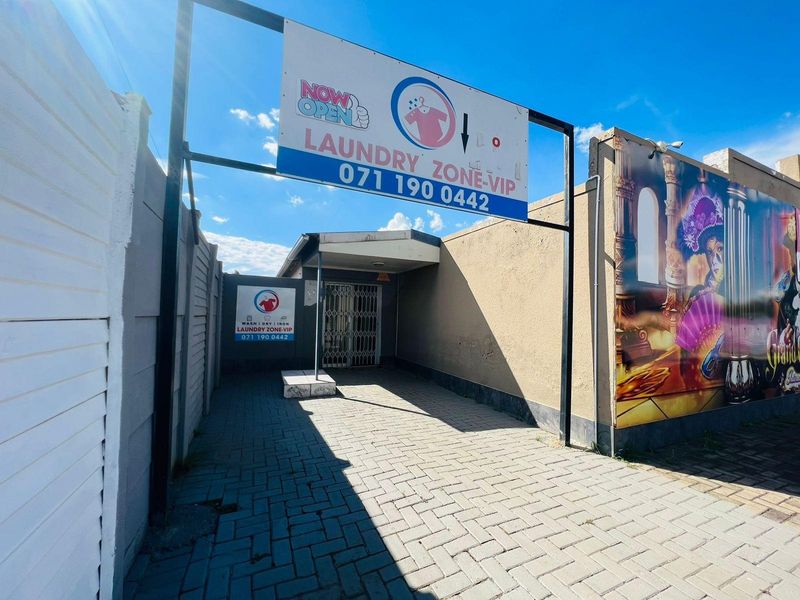 Exterior view of a commercial laundry facility entrance featuring paved access, security gate, and prominent business signage.