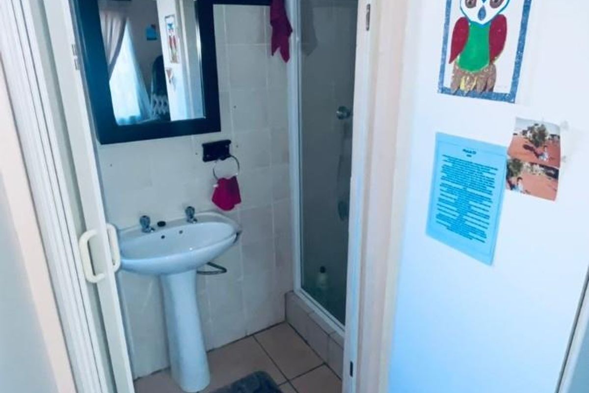 A compact bathroom featuring a pedestal basin, tiled walls, and a separate shower enclosure with a glass door.