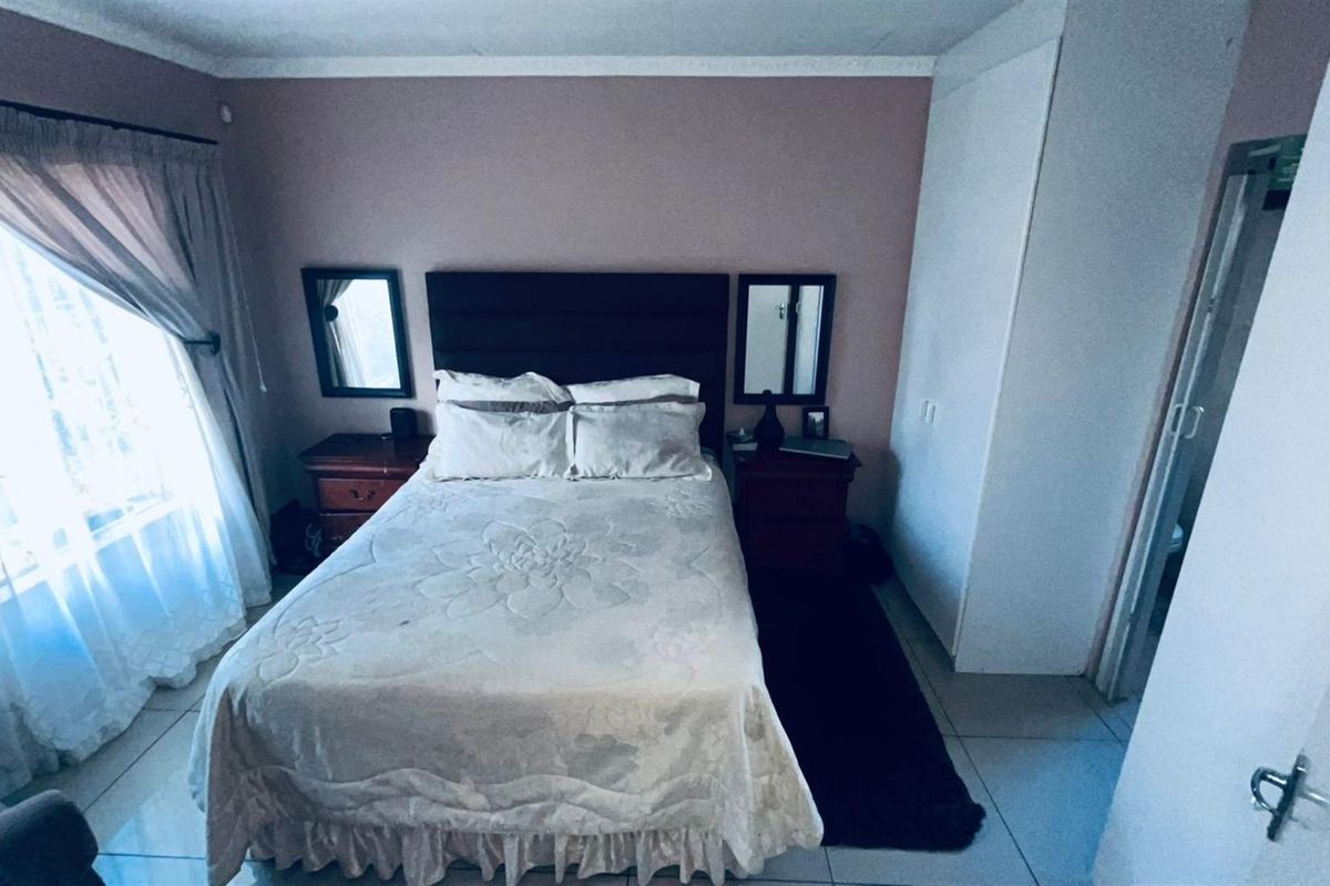 A bedroom featuring tiled flooring, built-in cupboards, and a window with curtains, providing a functional and comfortable living space.