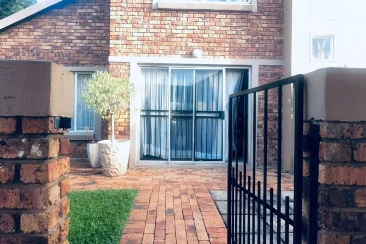 A rear exterior view featuring a face brick facade, a brick paved walkway leading to sliding glass doors, and a secure metal gate.