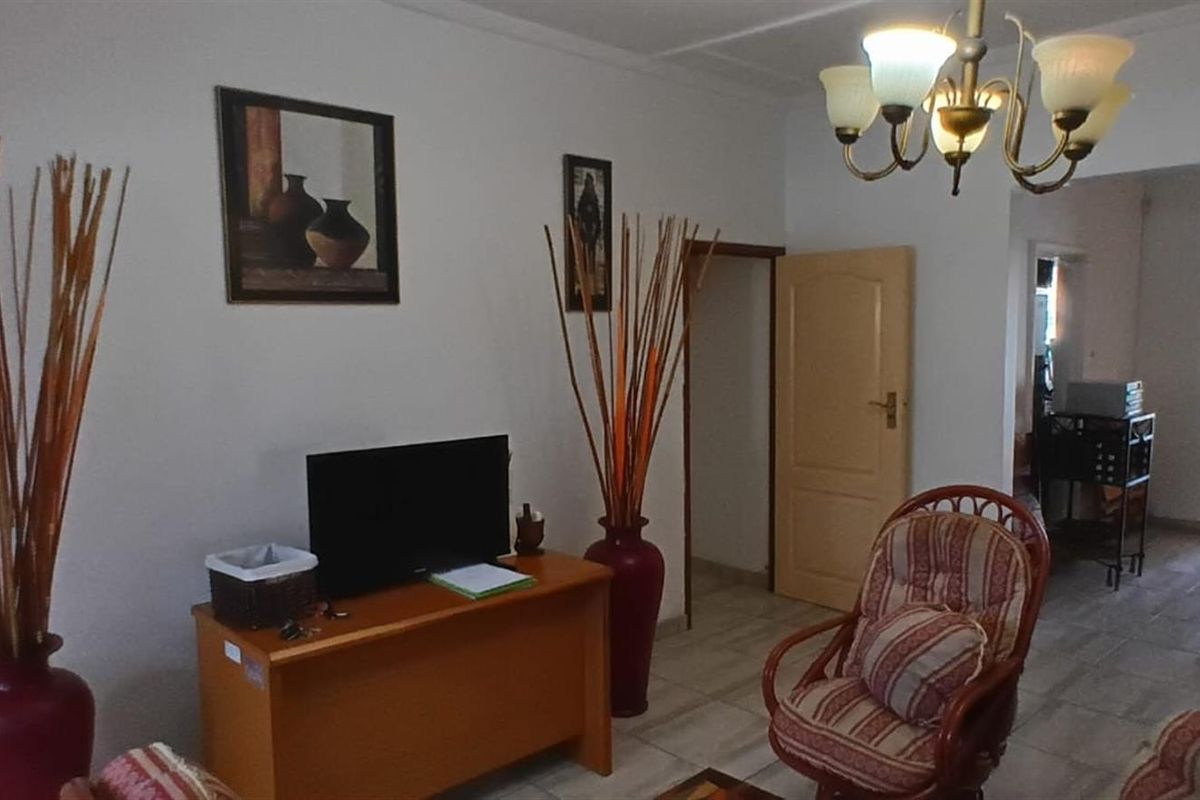 A living room area featuring tiled flooring and a central chandelier, providing access to adjacent rooms.