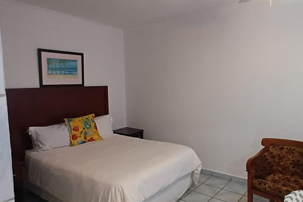 A simple bedroom featuring tiled flooring and a ceiling fan, providing a functional and clean space for guests.
