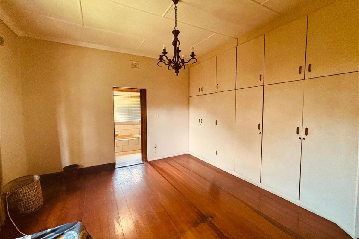 A spacious bedroom featuring polished timber flooring, extensive floor-to-ceiling built-in cabinetry, and direct access to an adjoining bathroom.