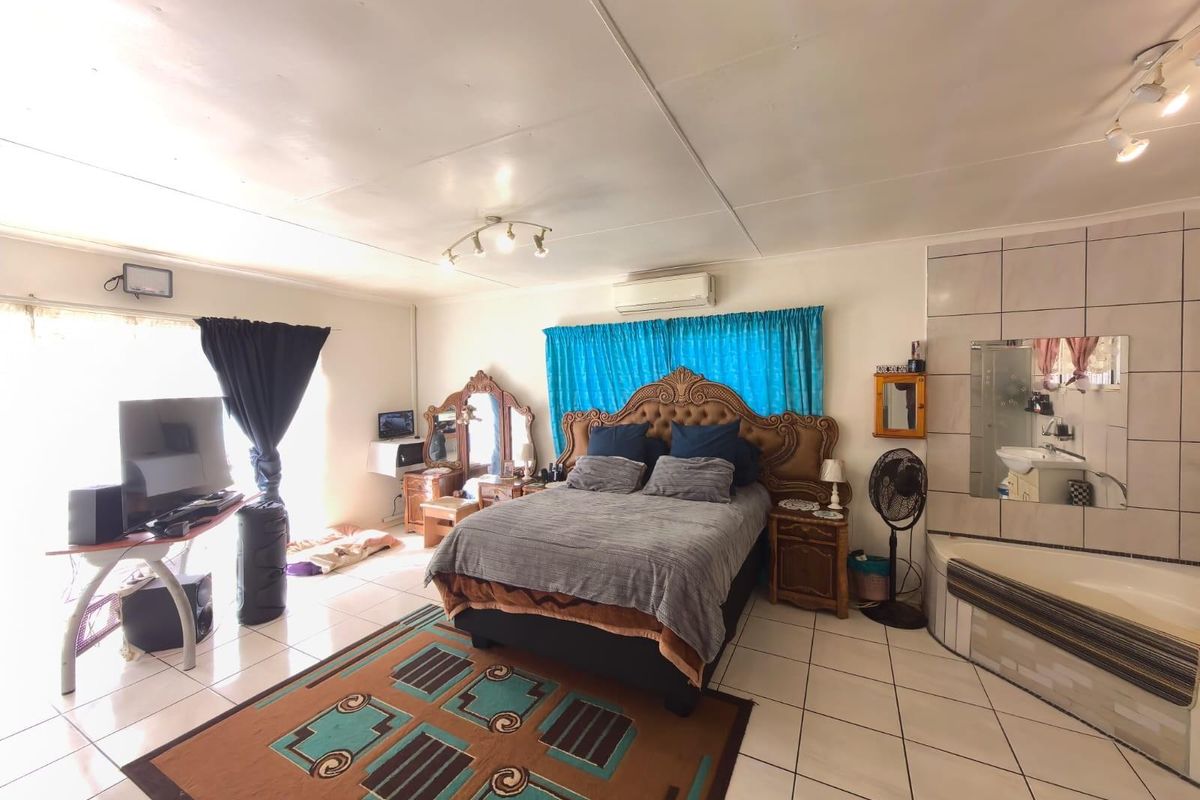 Spacious bedroom featuring tiled flooring, an integrated corner bathtub with tiled surround, and a wall-mounted air conditioning unit.