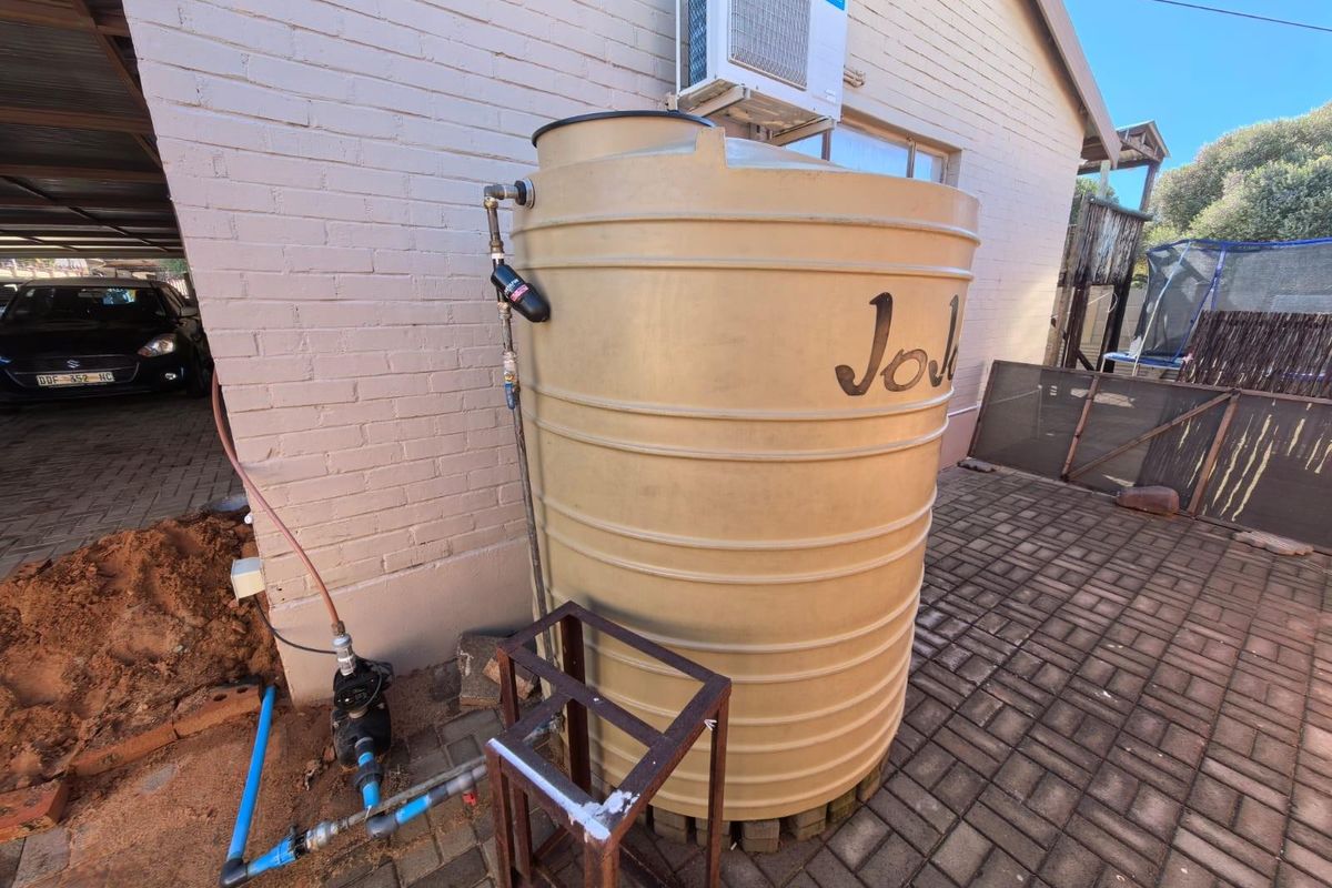 Exterior view showing a large water storage tank with integrated pump system and wall-mounted air conditioning unit.