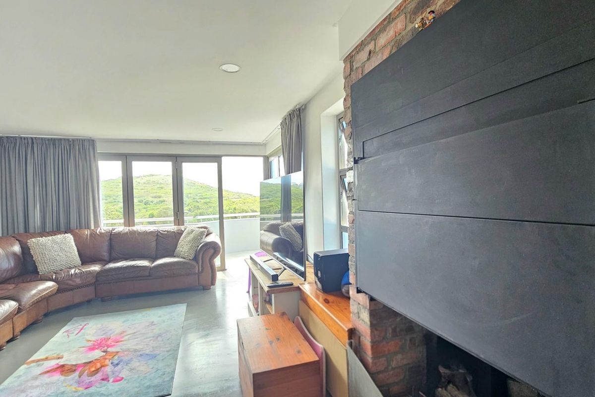 A living room featuring a prominent brick fireplace with a black metal insert, large glass sliding doors leading to a balcony, and polished concrete flooring.