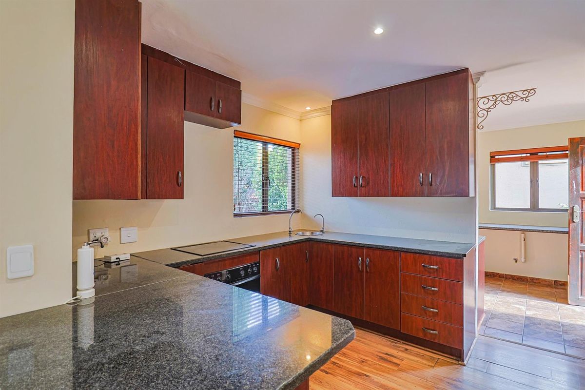 A functional kitchen featuring dark wood cabinetry, granite countertops, a built-in oven, and an electric hob, with natural light from a window.