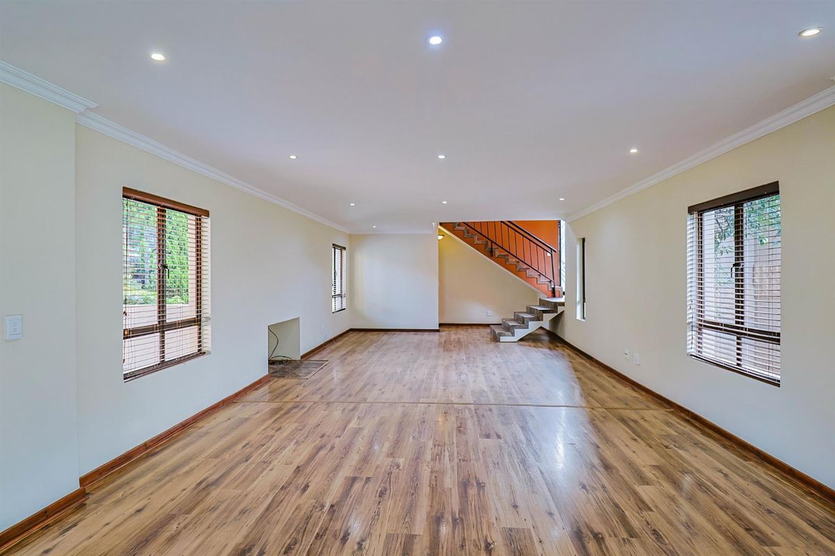 Spacious open-plan living area featuring laminate flooring, recessed lighting, a fireplace hearth, and a staircase with a metal railing.