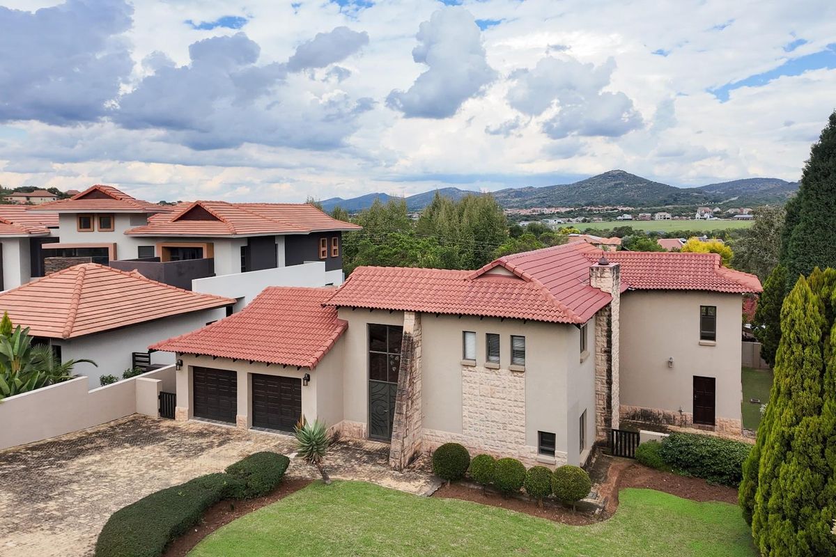 Aerial view of a residential property featuring a terracotta tile roof, stone-clad facade, double garage, and a well-maintained garden with scenic mountain views.