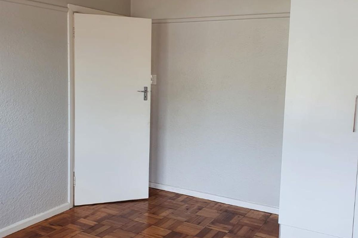 A bright bedroom featuring polished parquet wooden flooring, neutral wall finishes, and a built-in wardrobe.