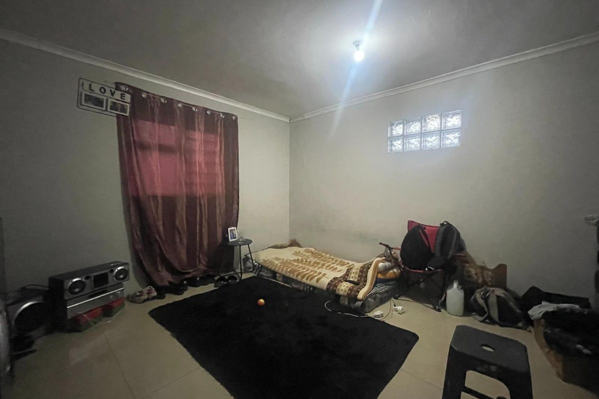 A bedroom featuring tiled flooring, a small glass block window, and coved ceiling detailing, offering a blank canvas for potential renovation and interior design updates.