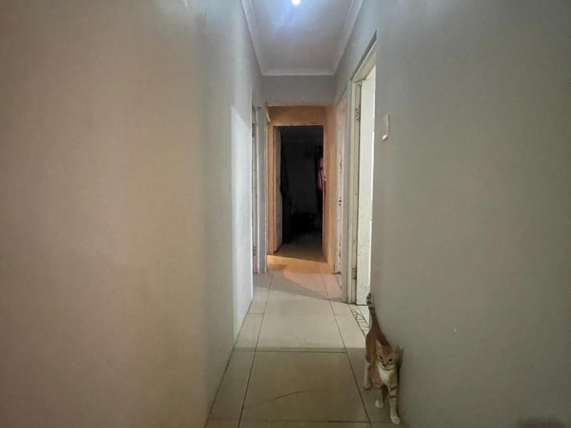 A narrow residential hallway featuring tiled flooring and simple cove cornicing, leading to multiple doorways.