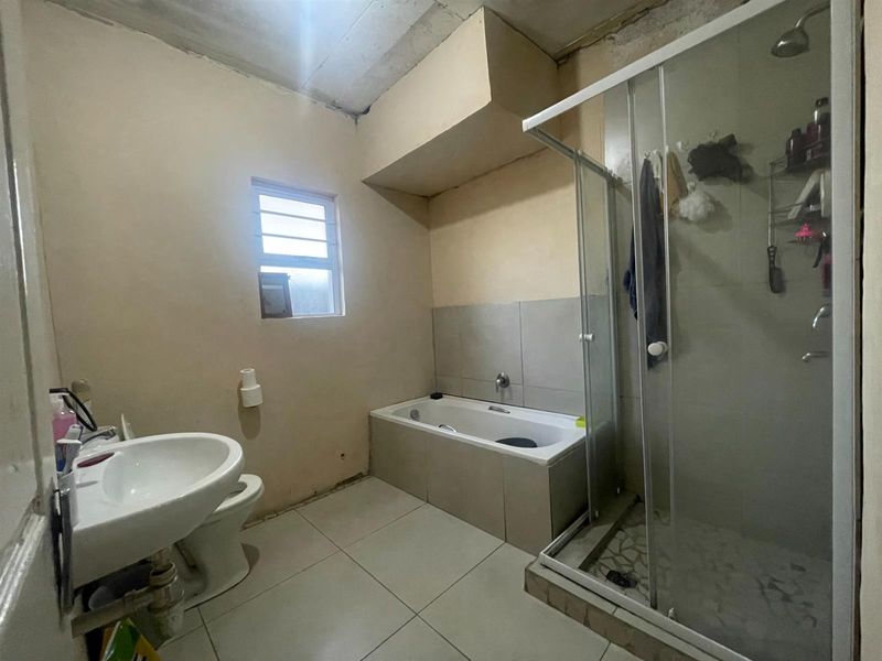 A functional bathroom featuring a built-in bathtub, separate shower enclosure, pedestal basin, and toilet, requiring cosmetic updates and finishing touches.