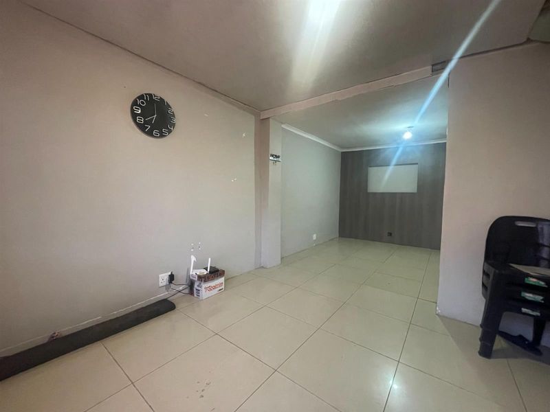 An open-plan living area featuring neutral tiled flooring, recessed lighting, and a dark wood-look accent wall, offering a blank canvas for interior design.