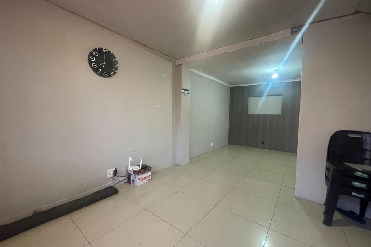 An open-plan living area featuring neutral tiled flooring, recessed lighting, and a dark wood-look accent wall, offering a blank canvas for interior design.