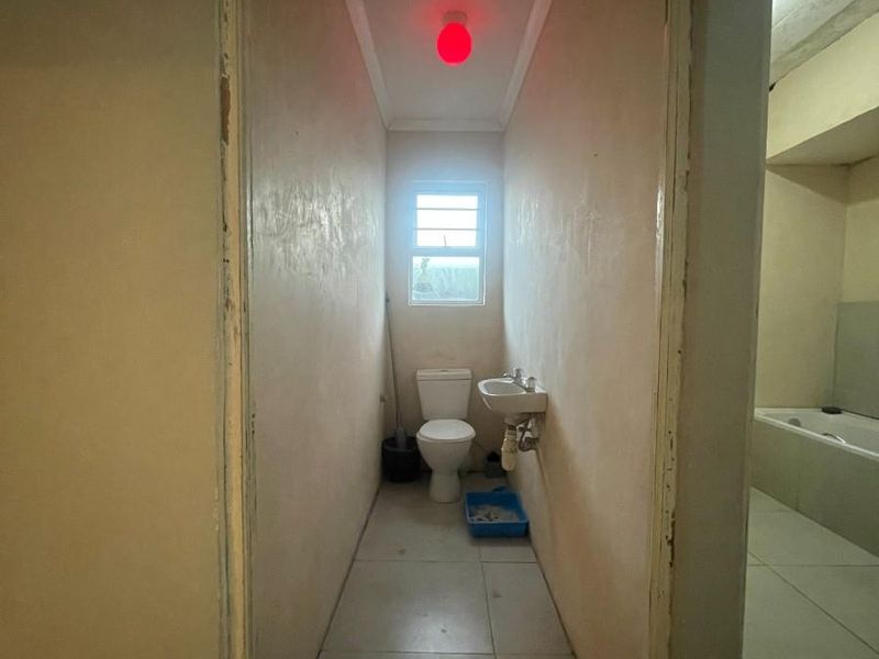 A compact bathroom featuring a toilet and wall-mounted basin with tiled flooring and a window for natural light.