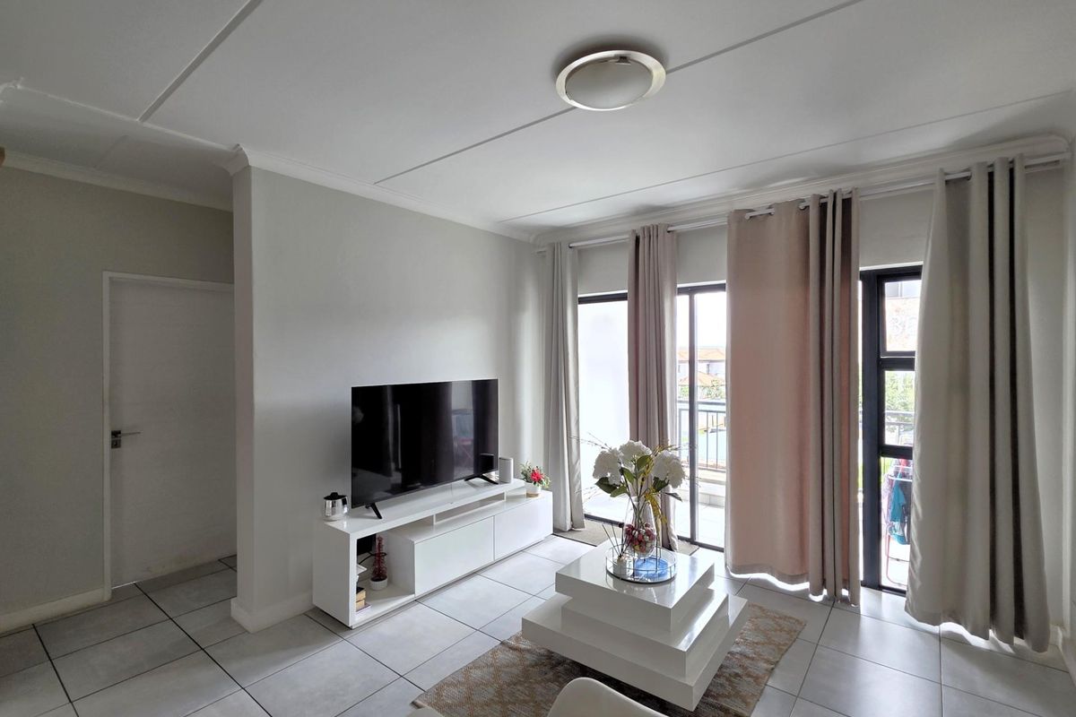 A bright and modern living room featuring neutral tiled flooring, large glass sliding doors leading to a balcony, and clean, well-maintained wall finishes.