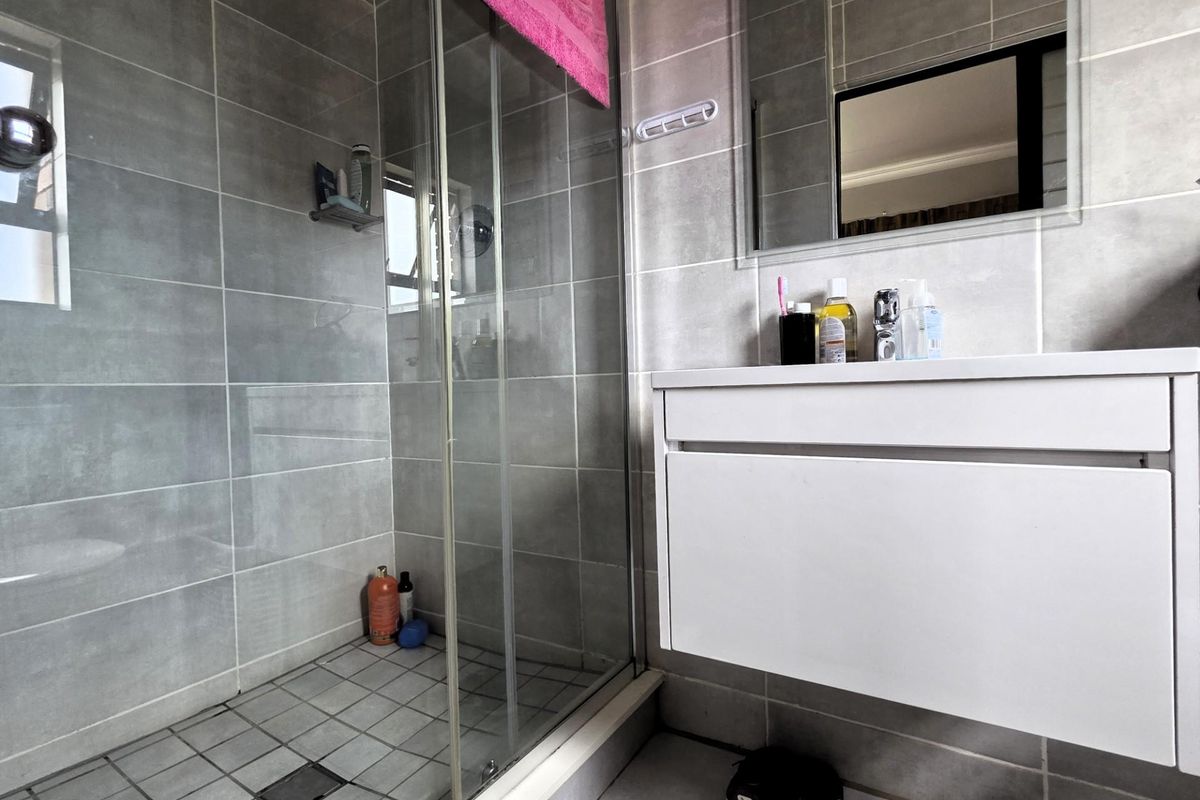 Modern bathroom featuring a glass-enclosed shower with grey wall tiles and a wall-mounted vanity unit with a mirror.