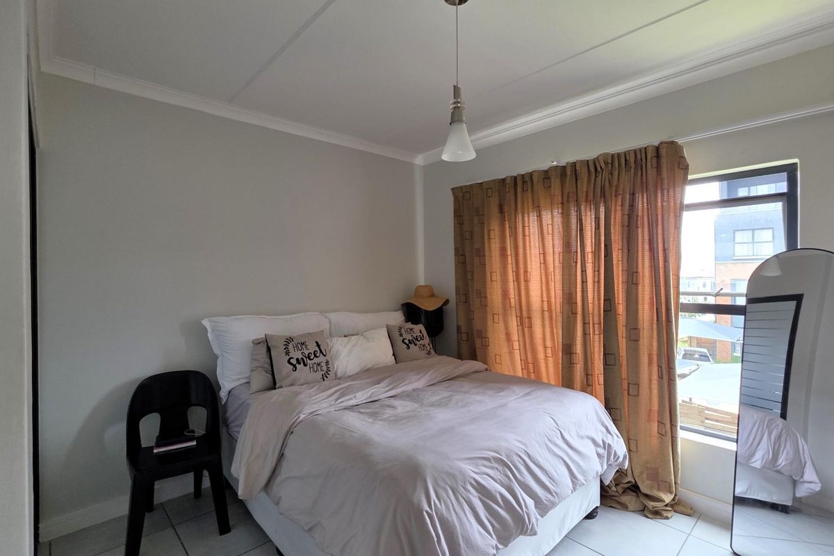 A functional bedroom featuring tiled flooring, a pendant light fixture, and a window with curtain treatments.