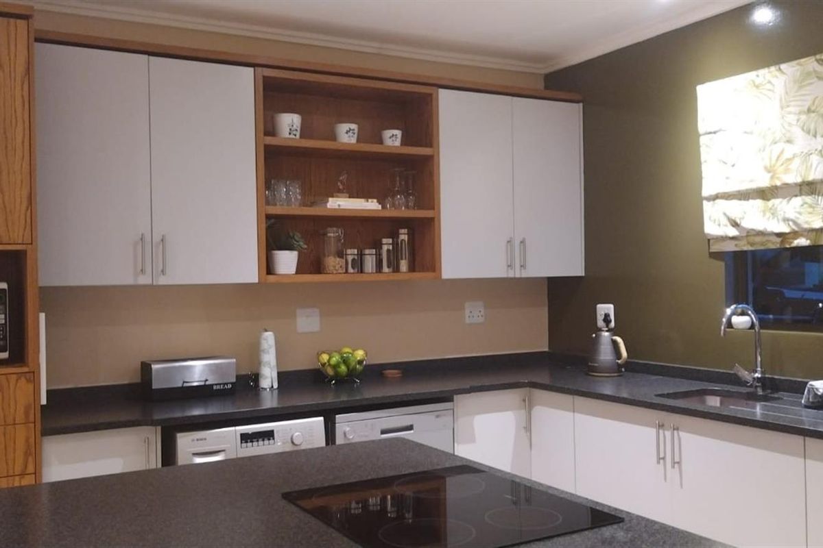 A functional kitchen featuring a central island with a built-in electric hob, dark countertops, and a mix of wood-grain and white cabinetry.