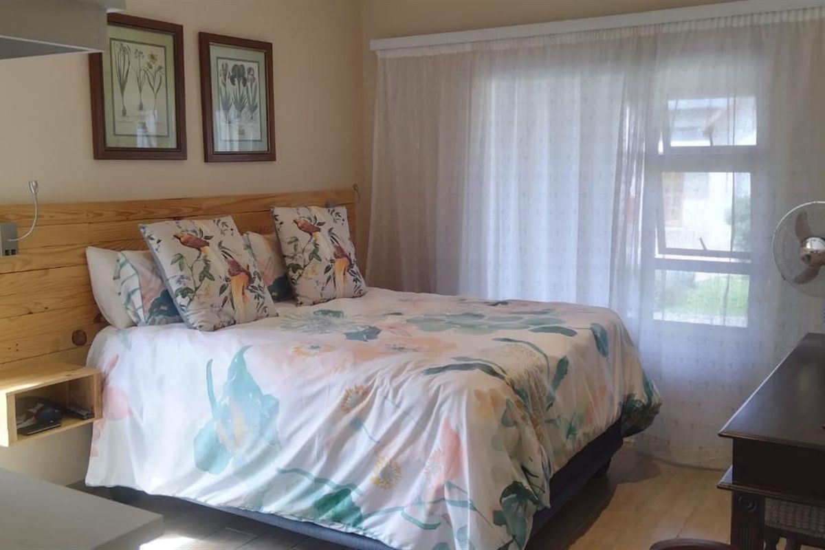 A comfortable bedroom featuring a built-in timber headboard with integrated shelving and large windows allowing for natural light.