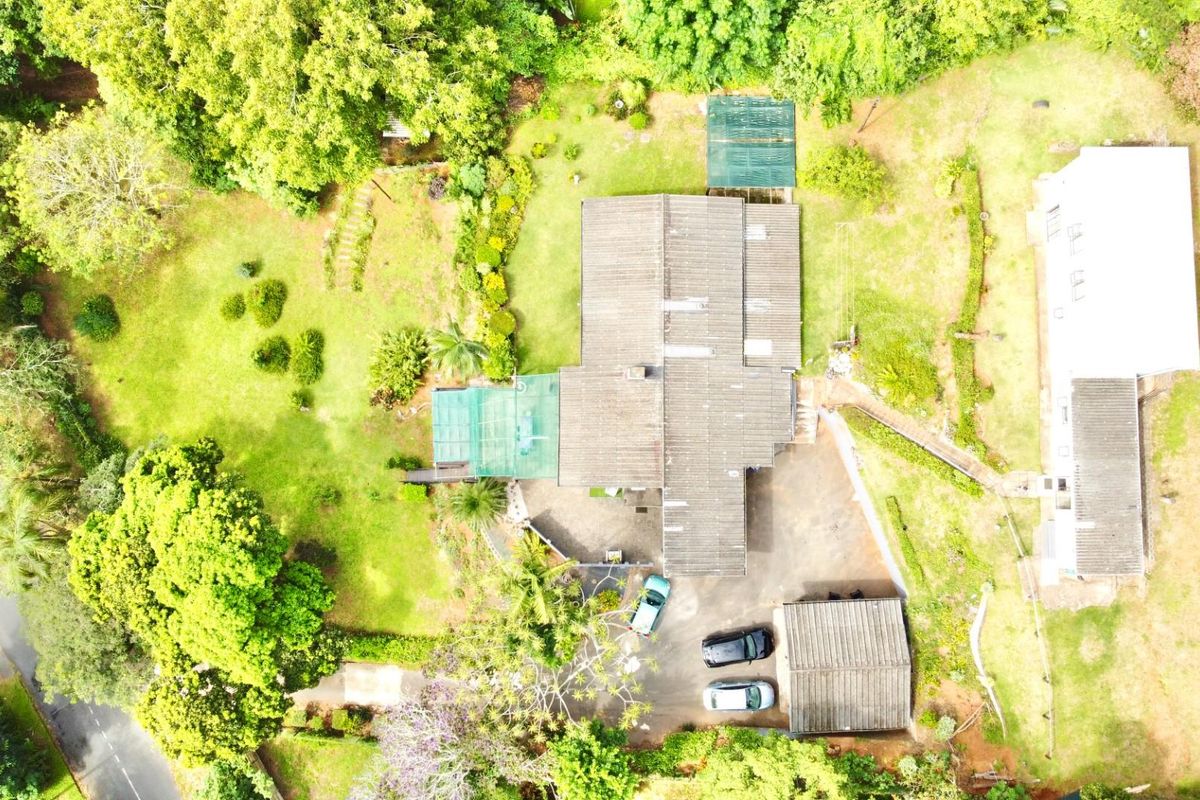 Aerial view of a residential property featuring a main dwelling, detached garage, and expansive landscaped garden grounds.