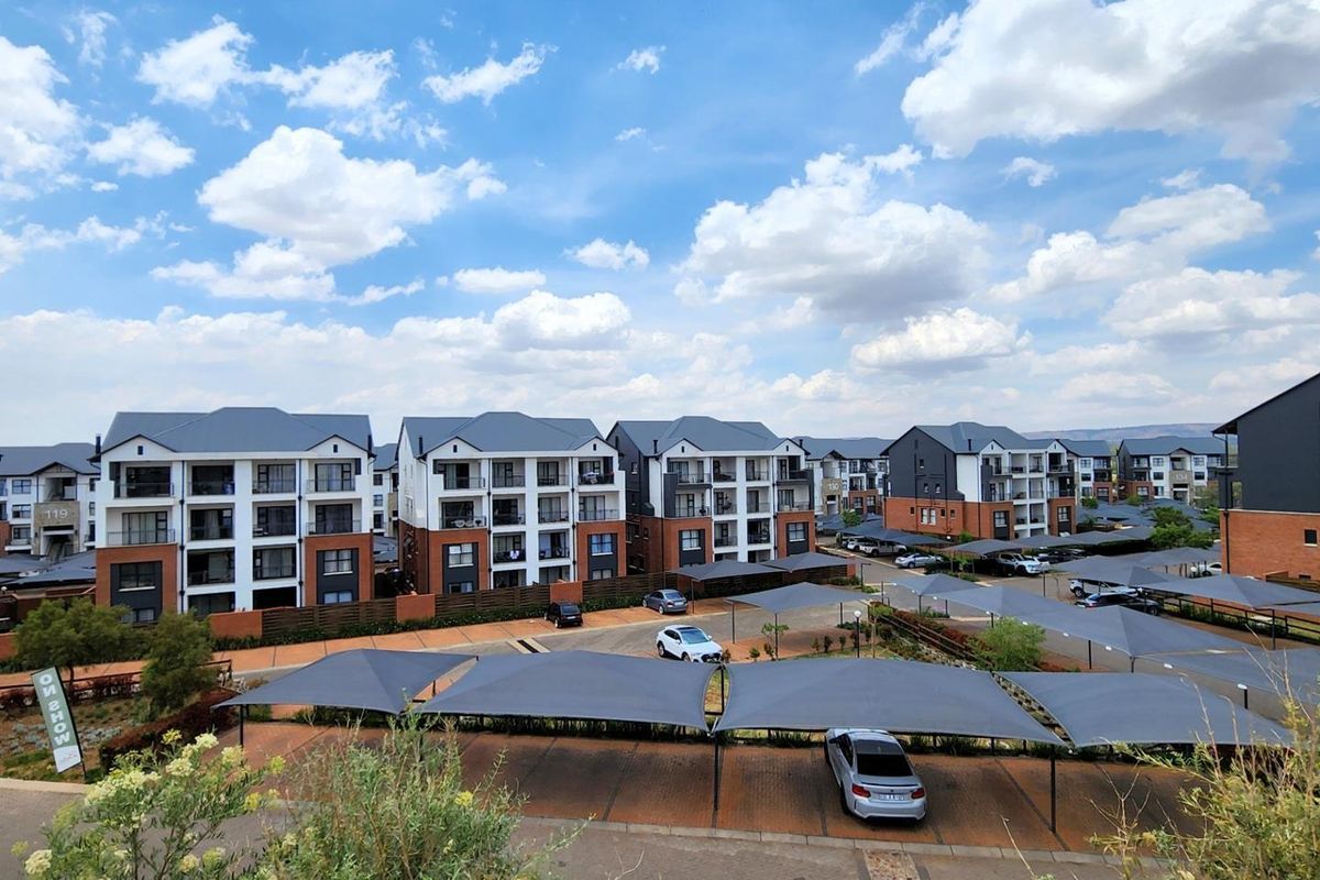 An elevated view of a modern apartment complex featuring multi-story residential buildings, paved parking areas, and covered shade-cloth carports.