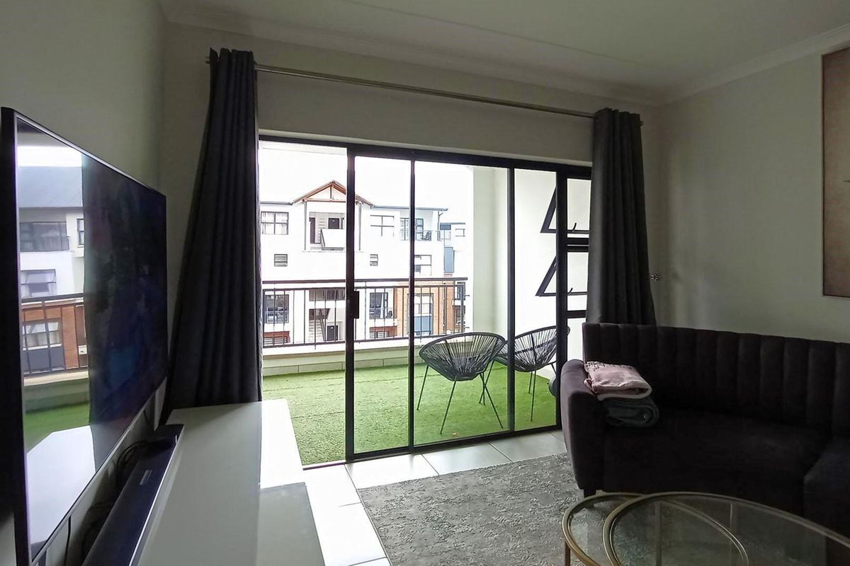 A bright living room featuring large sliding glass doors that open onto a private balcony with artificial turf.