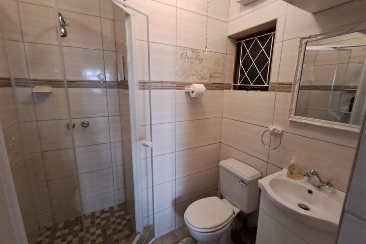 Compact bathroom featuring a glass-enclosed shower, pedestal basin, and toilet with neutral wall tiling and a small window for ventilation.