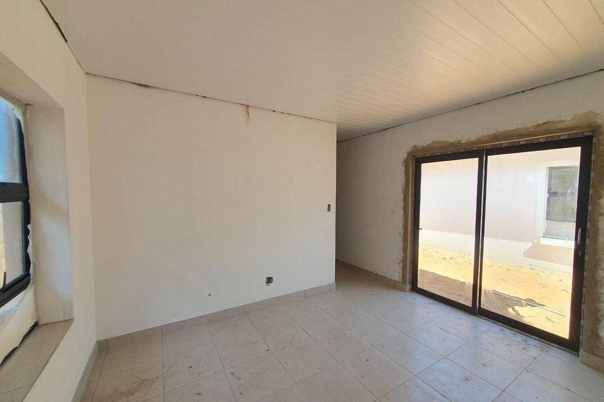 An empty, unfinished room featuring tiled flooring, a sliding glass door leading to the exterior, and a white paneled ceiling.