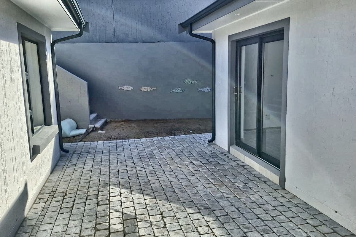 A paved courtyard area situated between two building wings, featuring sliding glass doors and a retaining wall with decorative accents.