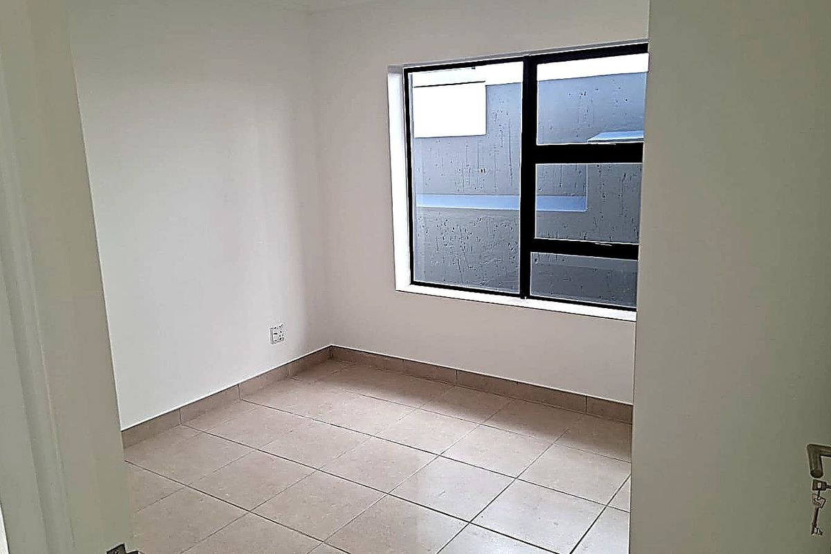 A bright, empty bedroom featuring neutral floor tiles and a large window with dark frames, offering a clean and versatile living space.