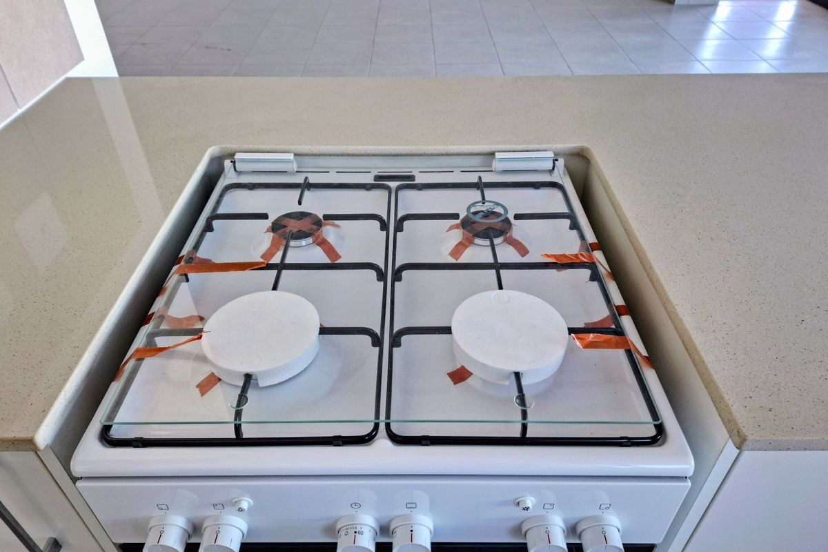 A clean, modern kitchen featuring a built-in gas hob with protective covers and a neutral stone-look countertop.