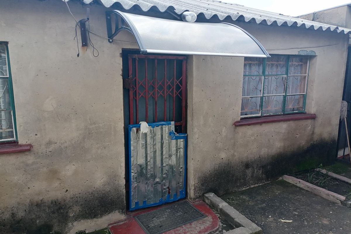 Exterior view of a residential building featuring a security gate, window burglar bars, and a protective door canopy.