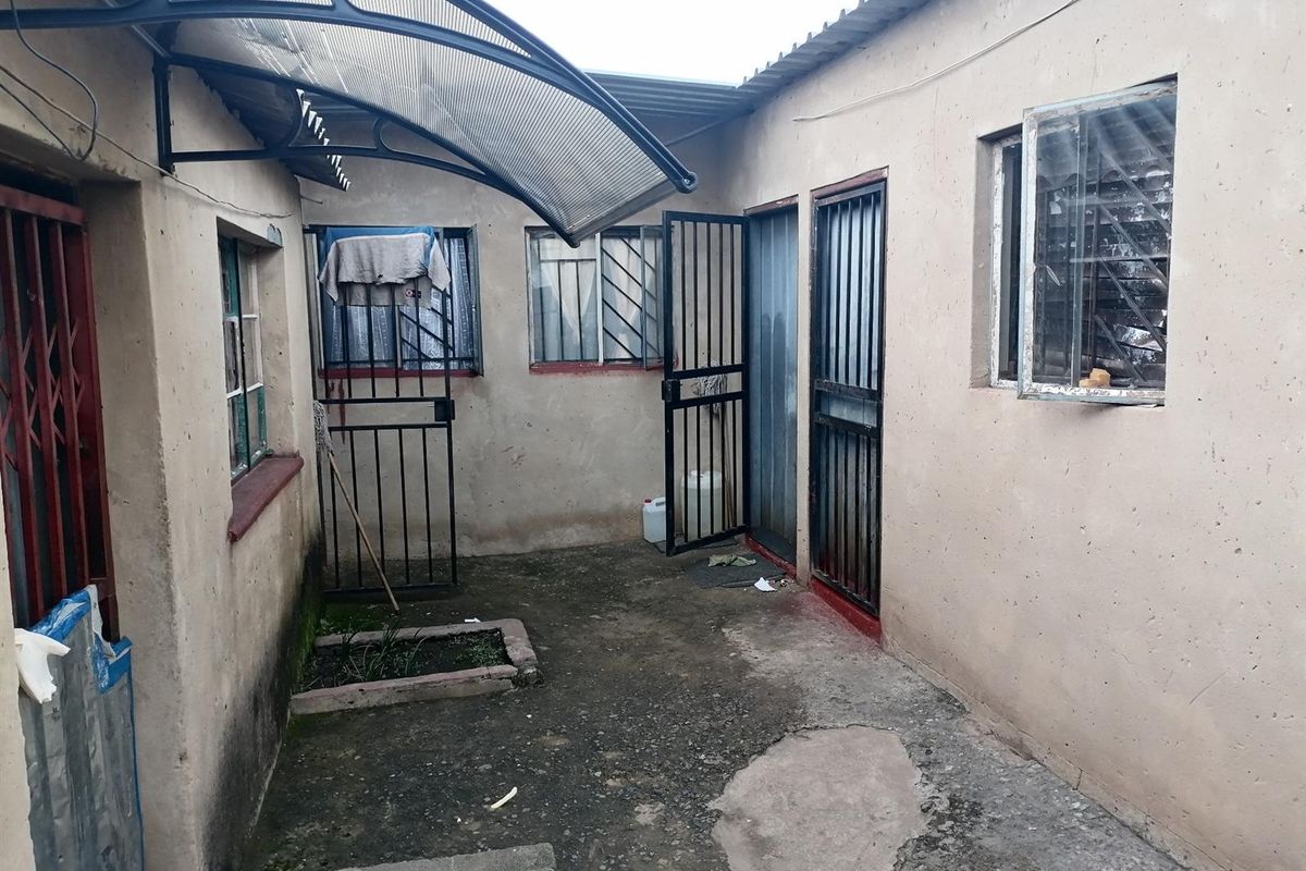 A rear exterior courtyard area featuring concrete paving, security gates, and a polycarbonate awning over the entrance.