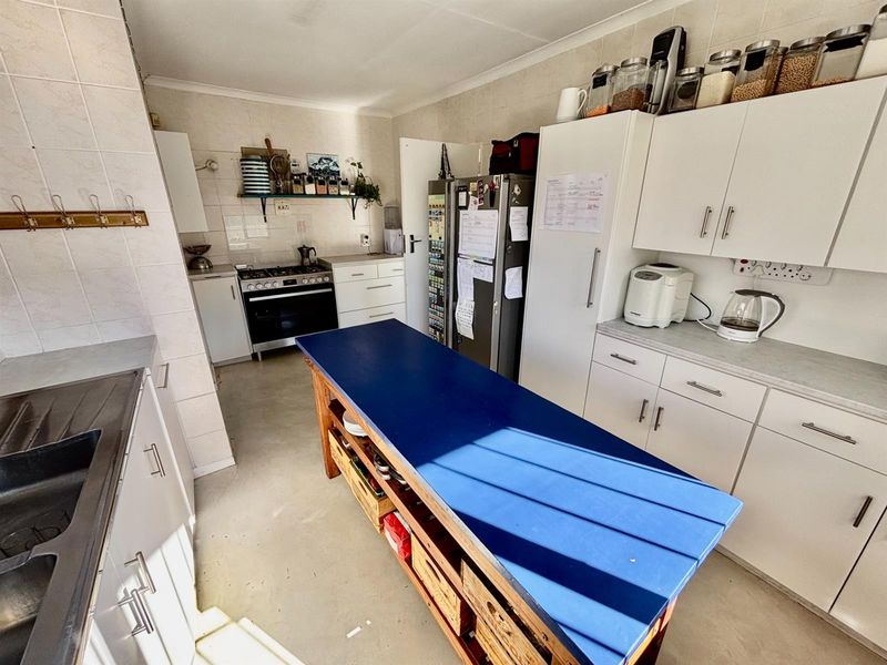 Functional kitchen featuring white cabinetry, tiled splashbacks, a gas stove with oven, and a central blue-topped island unit.