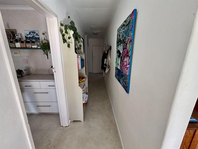 A functional hallway connecting to a kitchen area, featuring neutral wall finishes, tiled flooring, and built-in cabinetry for storage.
