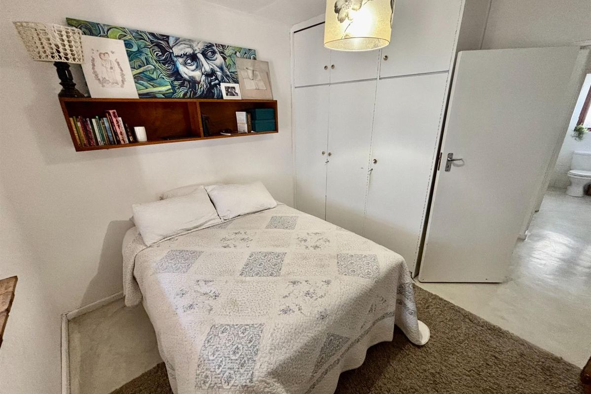 A functional bedroom featuring built-in cupboards and a floating wall shelf, with direct access to an adjacent bathroom.