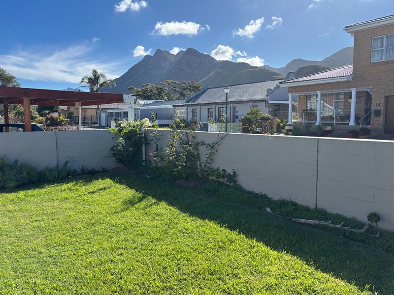 A private rear garden featuring a well-maintained lawn, a concrete block boundary wall, and a timber pergola with scenic mountain views.