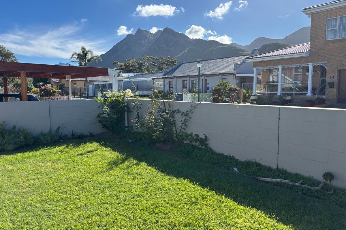 A private rear garden featuring a well-maintained lawn, a concrete block boundary wall, and a timber pergola with scenic mountain views.