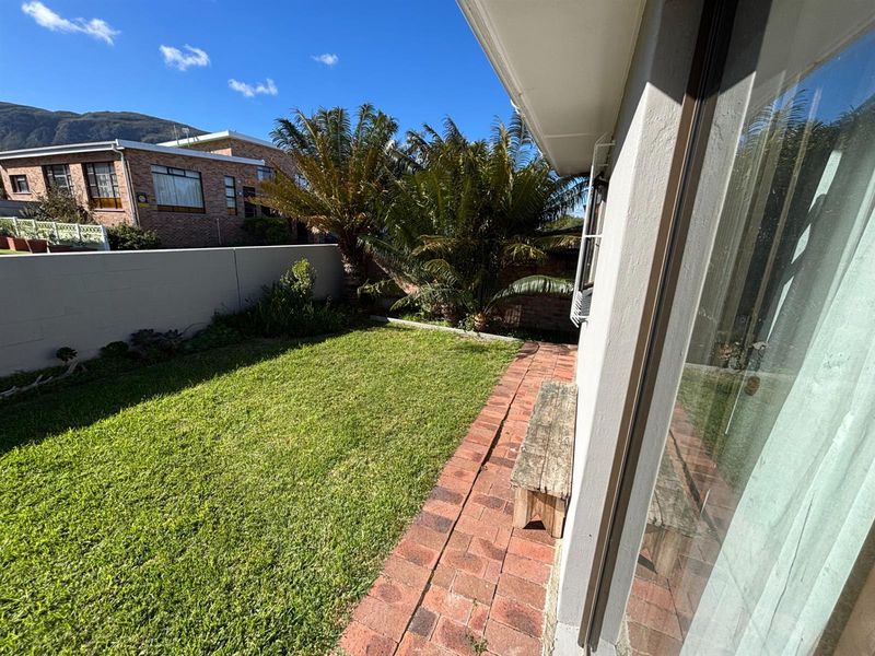 A private rear garden featuring a lawn area, brick paved pathway, and a boundary wall, accessible via a large sliding glass door.