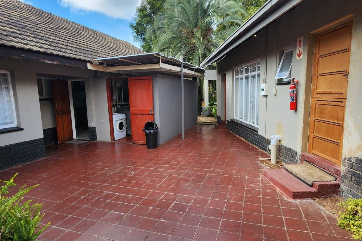 A paved rear courtyard area connecting multiple building sections, featuring tiled flooring, exterior access doors, and wall-mounted safety equipment.