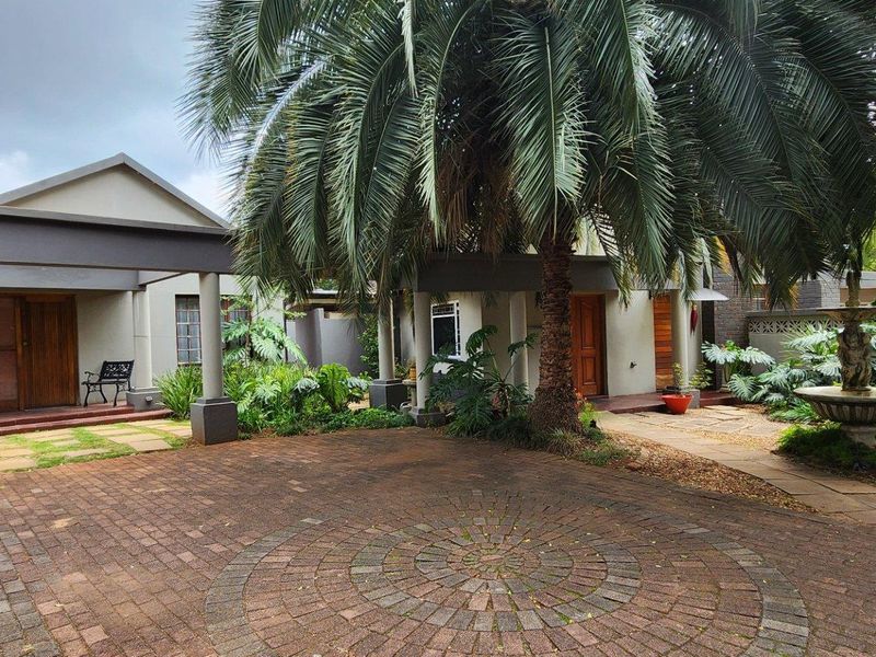 Front exterior view of the guest house featuring a circular paved driveway, covered entrance, mature palm tree, and a decorative stone fountain.