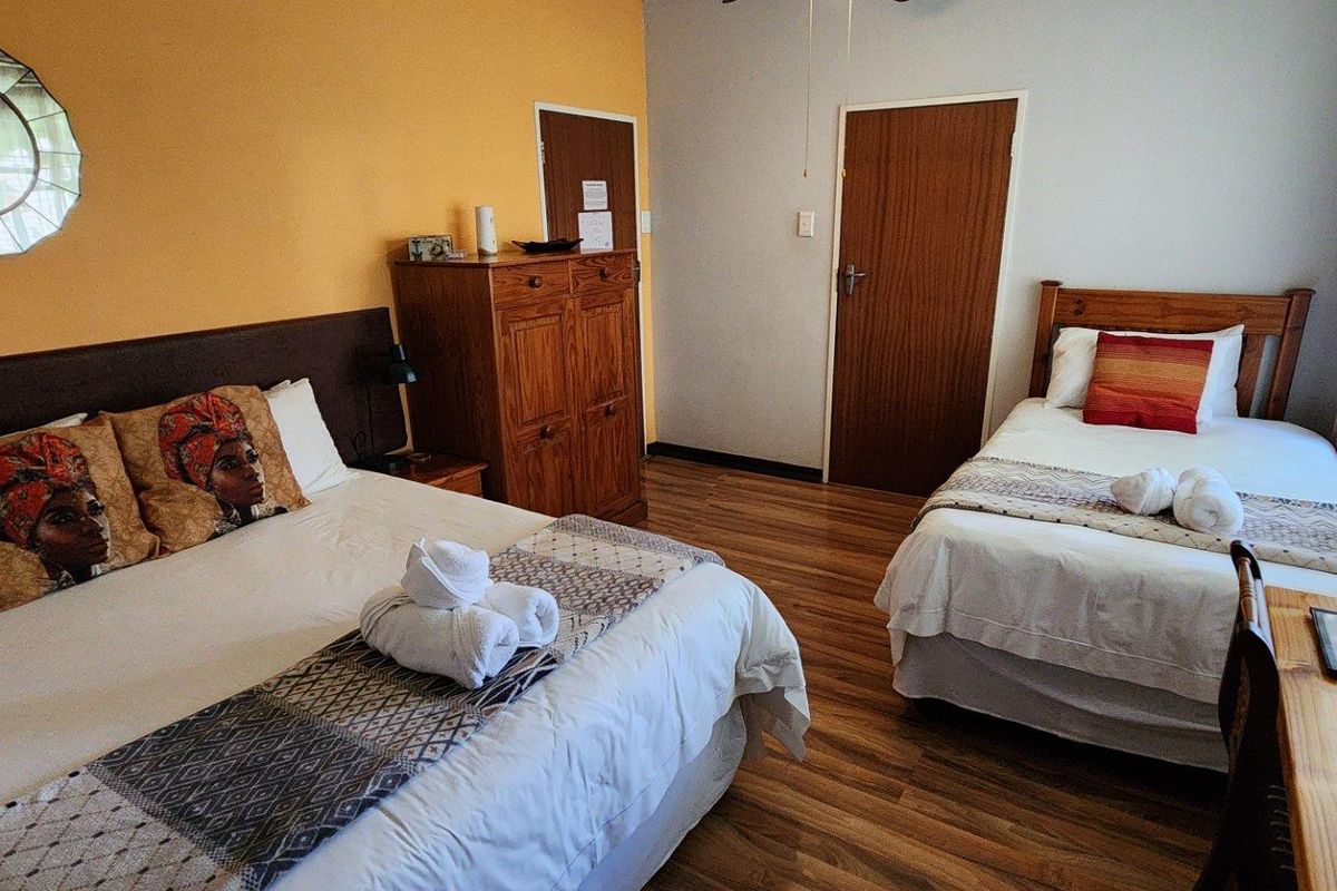 A guest bedroom featuring laminate flooring, a ceiling fan, and two beds, providing a functional space for guests.