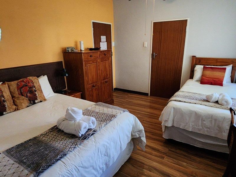 A guest bedroom featuring laminate flooring, a ceiling fan, and two beds, providing a functional space for guests.